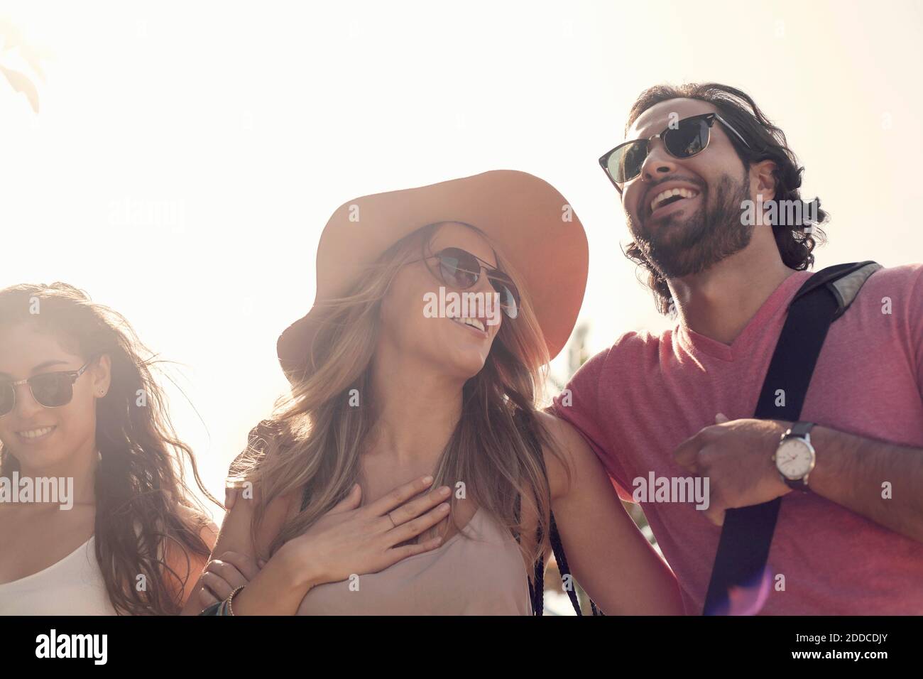 Lächelnde Freundinnen und Freundinnen in Sonnenbrillen sprechen gegen klar Himmel Stockfoto