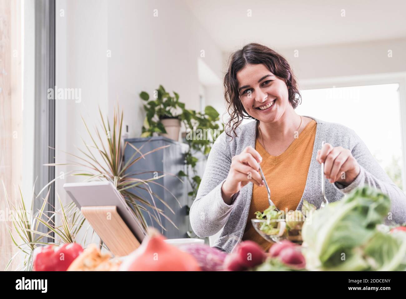 Lächelnde Frau essen Salat, während mit digitalen Tablet zu Hause Stockfoto