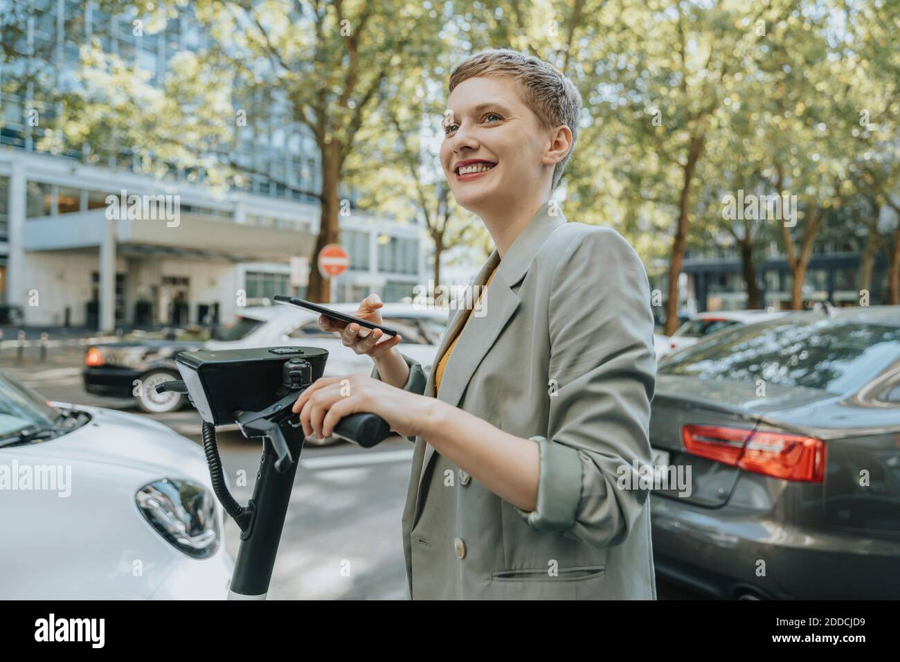 Frau entriegeln elektrische Push-Roller mit Smartphone im Stehen Auf der Straße in der Stadt Stockfoto