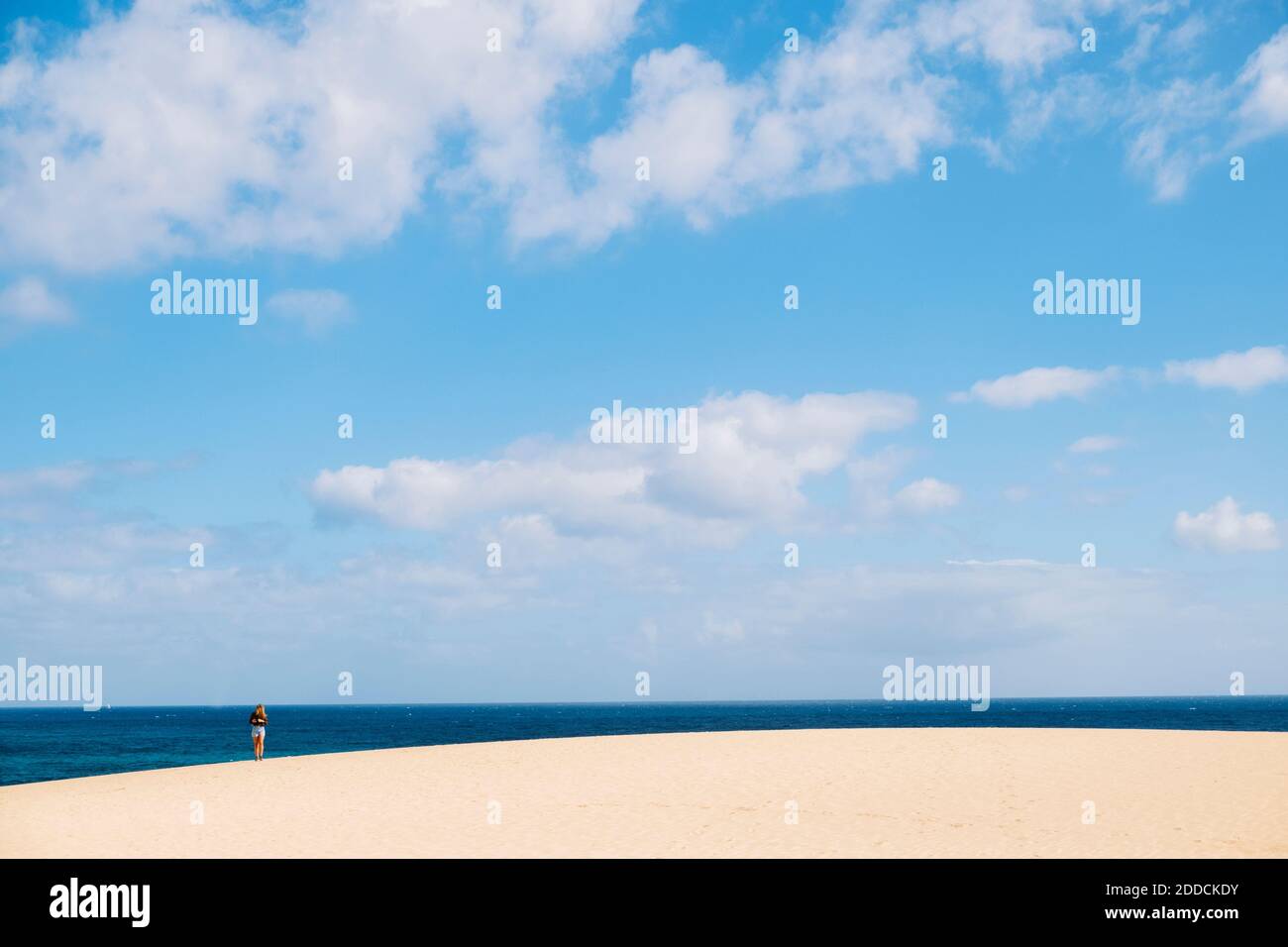 Fernansicht einer jungen Frau, die am Strand auf der Sonne steht Tag Stockfoto