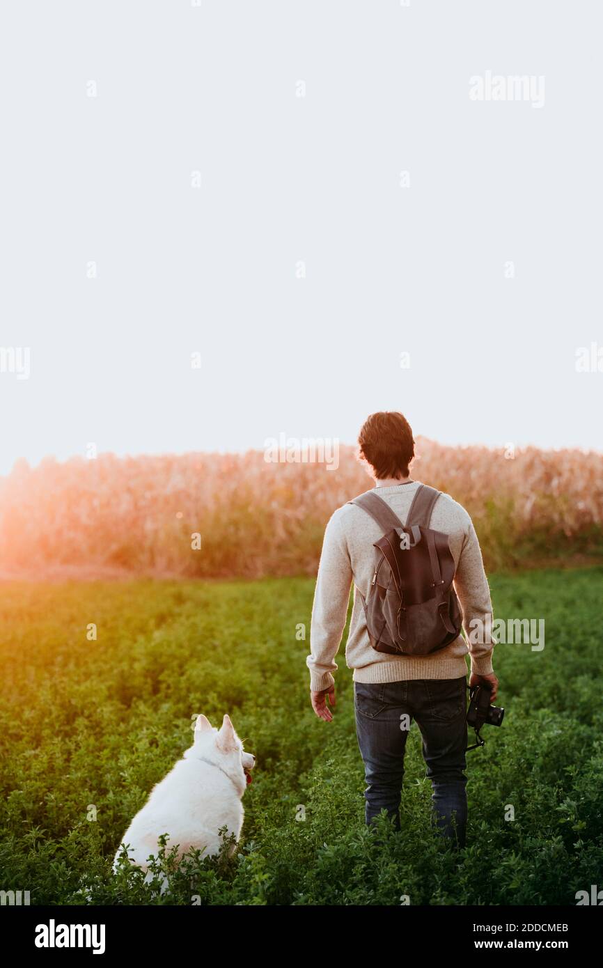 Mann mit Rucksack hält Kamera beim Schleifen von Hund an Ein Stockfoto