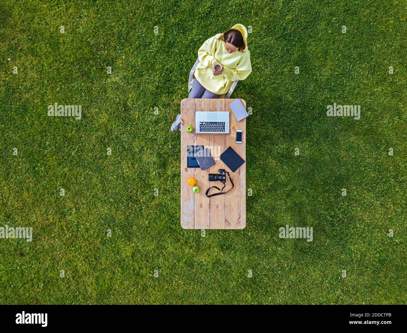 Luftaufnahme der Frau, die am Couchtisch sitzt Grüner Rasen mit Tasse Kaffee in den Händen Stockfoto