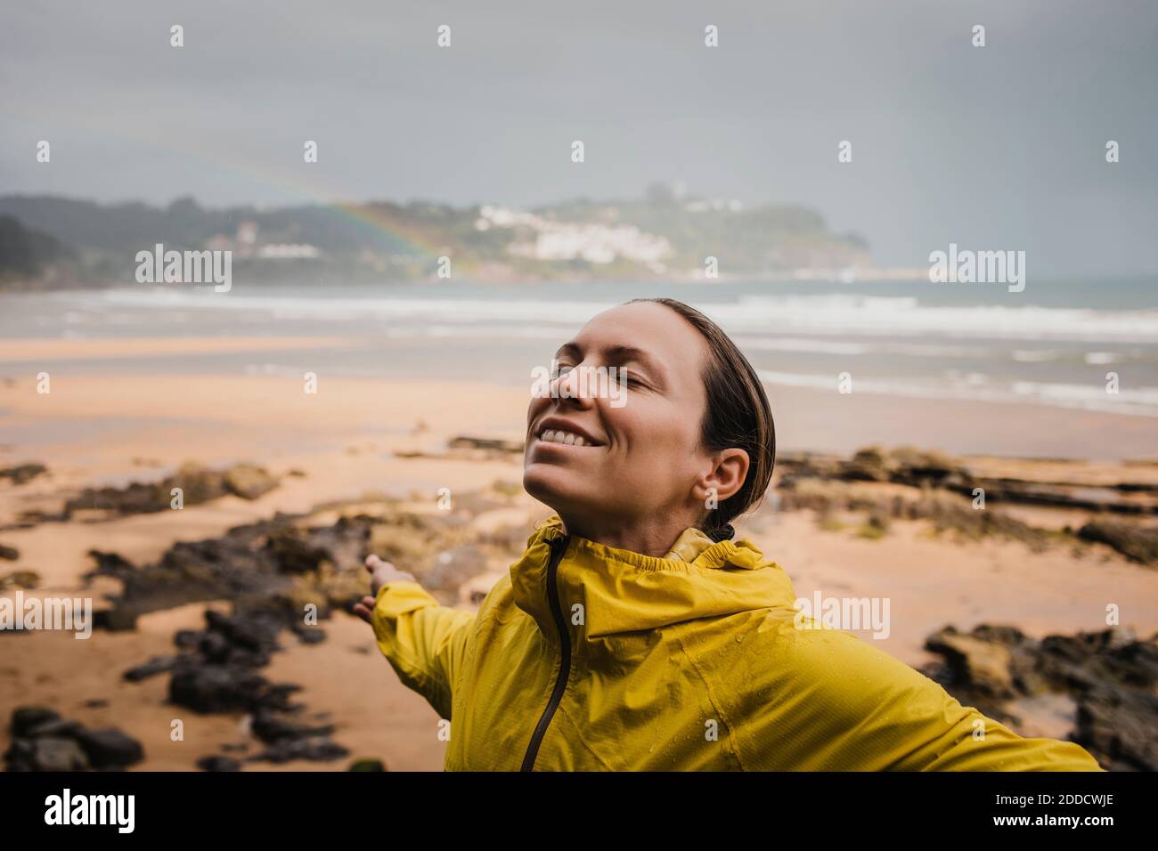Lächelnde Frau in Regenmantel am Strand während der Regenzeit Stockfoto