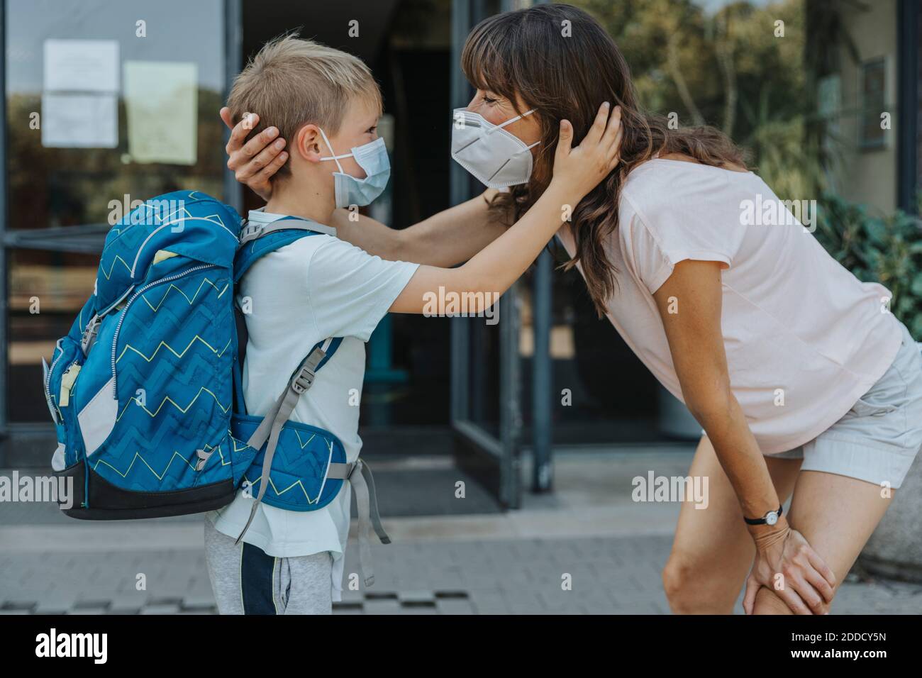 Mutter und Sohn tragen eine Schutzmaske, die von Angesicht zu Angesicht steht Vor dem Schulgebäude Stockfoto