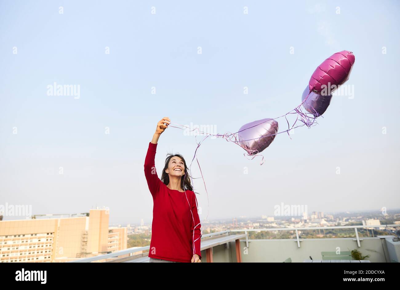 Lächelnde Frau mit einem Ballon in Herzform, der gegen den klaren Himmel steht Stockfoto