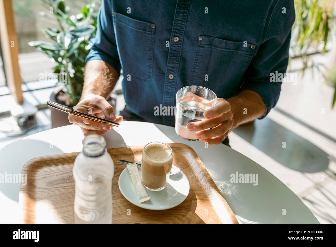 Geschäftsmann mit Smartphone, während Wasser im Glas trinken Tisch im Restaurant Stockfoto
