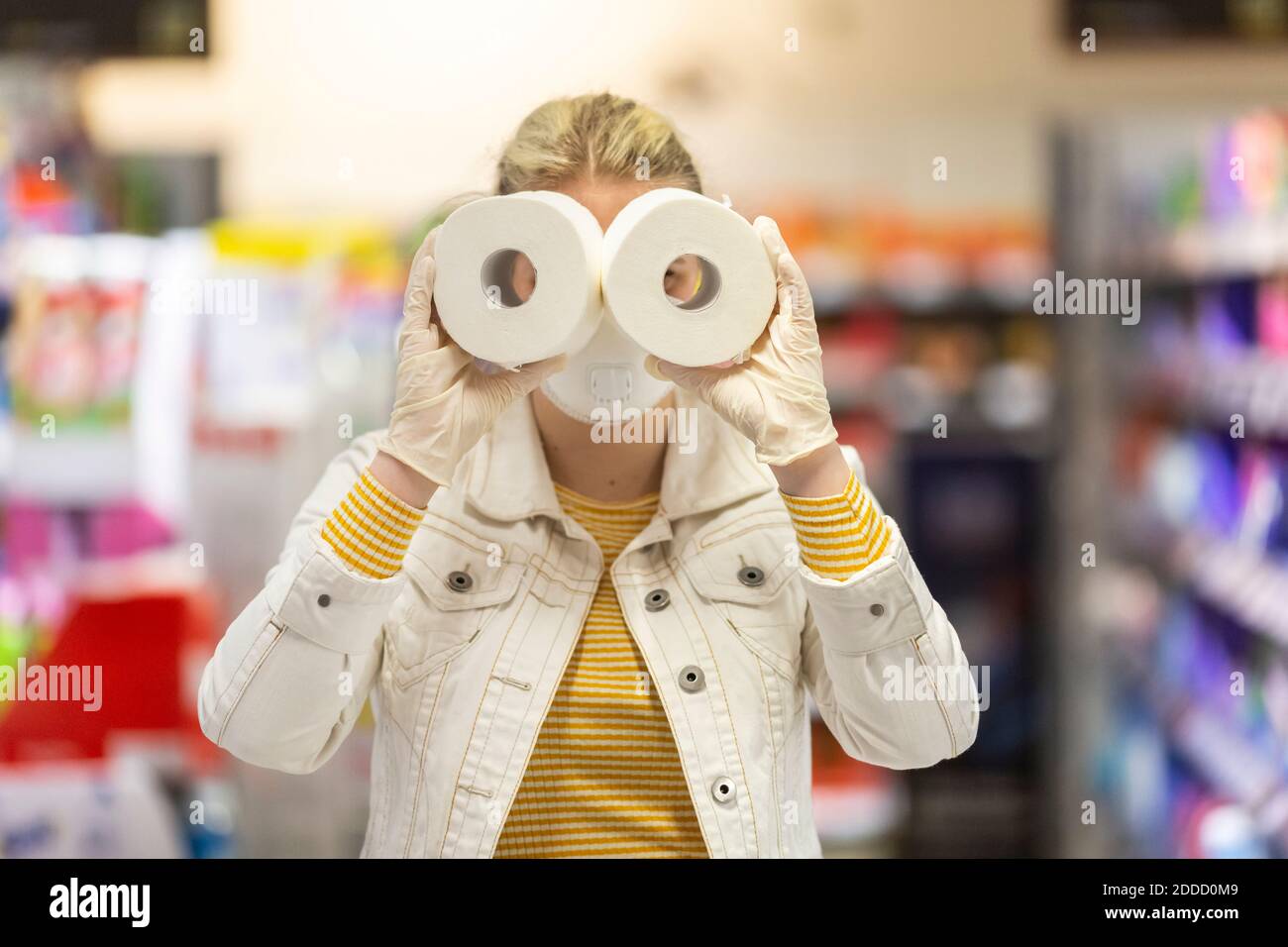 Teenager-Mädchen tragen Schutzmaske und Handschuhe halten Blick durch Löcher von Toilettenrollen im Supermarkt Stockfoto