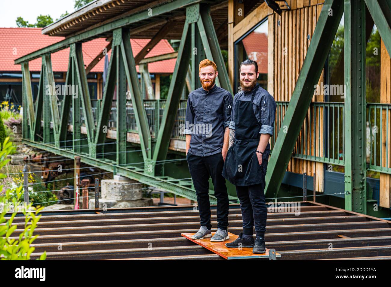 Chefs Alexander Gläsel (links) und Marcel Meining stehen an der Stelle, an der die offene Küche des Restaurants 'Brückenbaron' auf einer stillgelegten Stahlbrücke über den Fluss Main in Sonderhofen, Deutschland, gebaut werden soll. Das verglaste Innere der Brücke bietet Platz für etwa 25 Gäste in einem streng regionalen, industriellen Designkonzept. Stockfoto