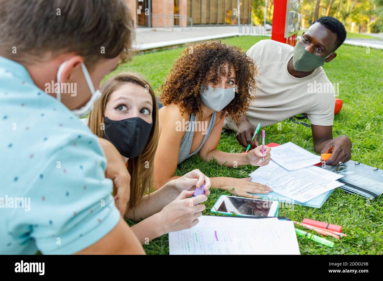 Männliche und weibliche Schüler tragen Sicherheitsmaske während der Diskussion auf Gras auf dem Universitätscampus Stockfoto