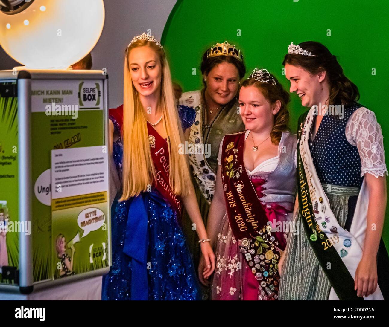 Vier gekrönte deutsche Lebensmittelköniginnen posieren lächelnd vor einer Fotokabine bei der Krönungszeremonie der Bayerischen Kartoffelkönigin 2019 in Schrobenhausen, Deutschland. Eine der Schleifen lautet „Rosenkönigin“. Stockfoto