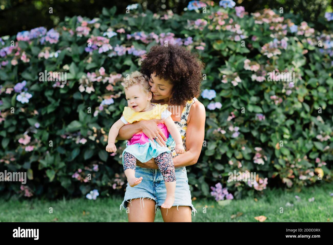 Mid adult Frau trägt Baby Mädchen, während sie gegen die Blüte stehen Anlage im Park Stockfoto
