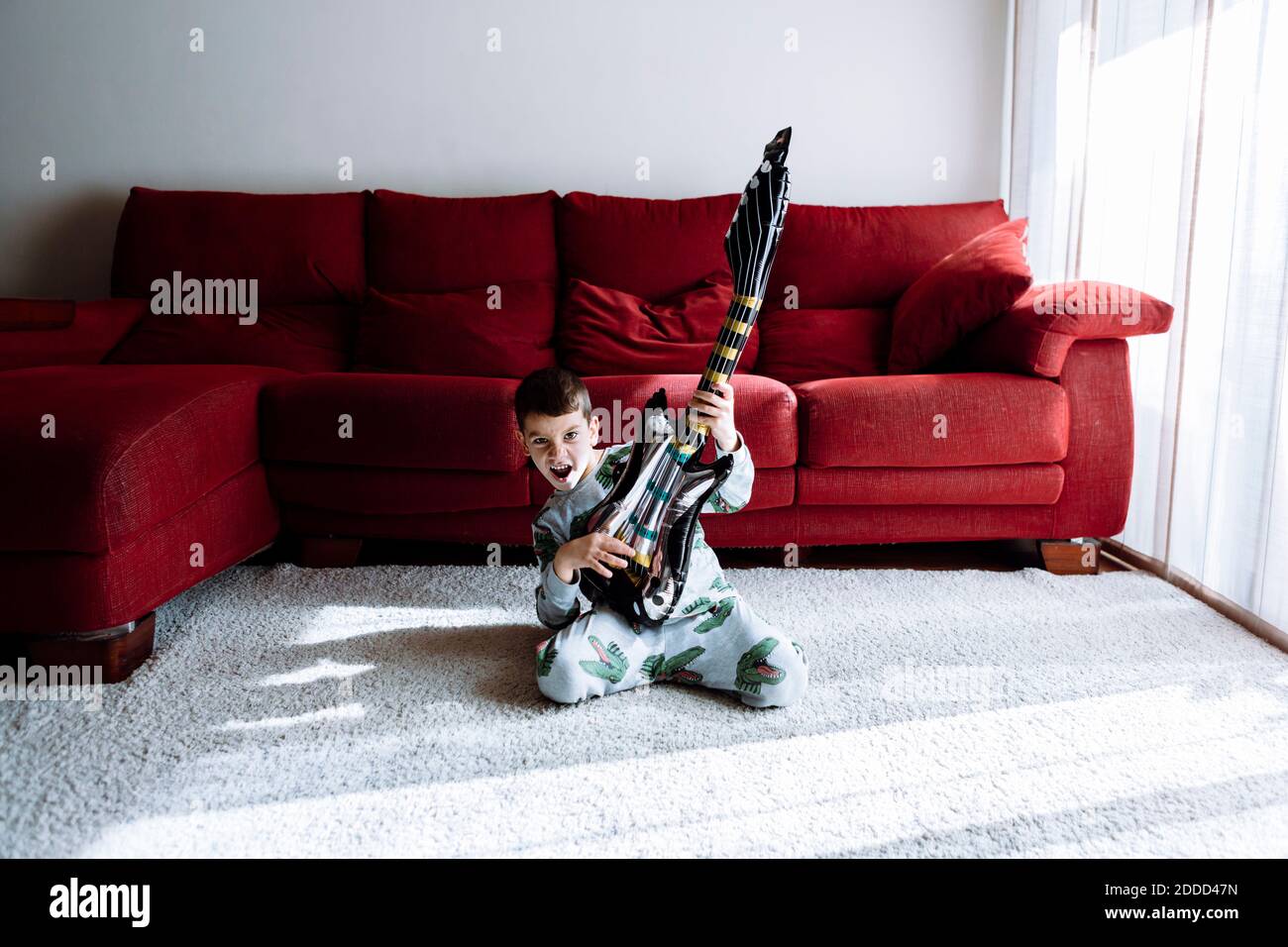 Glücklicher Junge Gitarre spielen, während kniete gegen Sofa im Leben Zimmer Stockfoto
