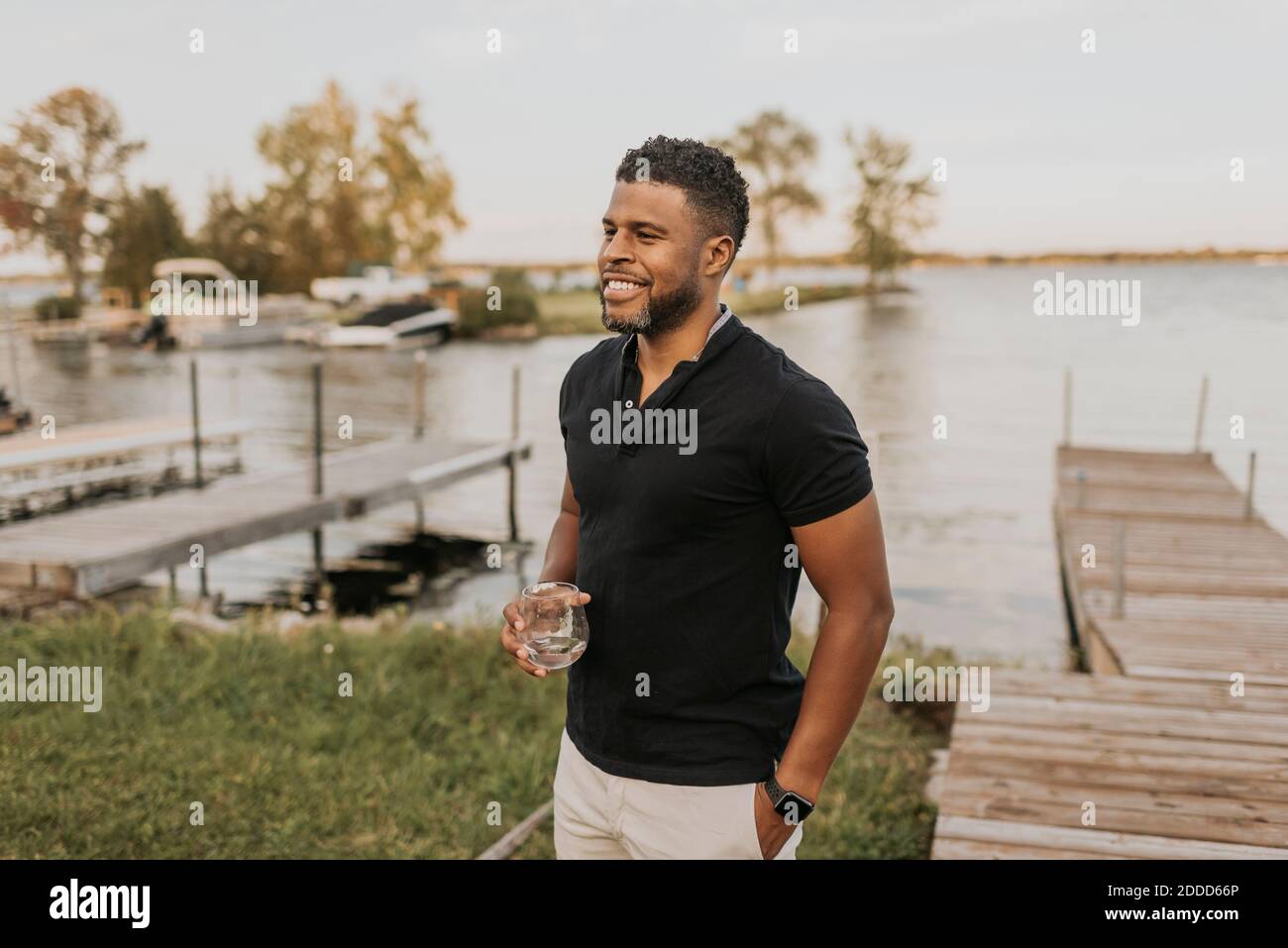 Lächelnder Mann steht mit Weinglas und Hand in der Tasche pier Stockfoto