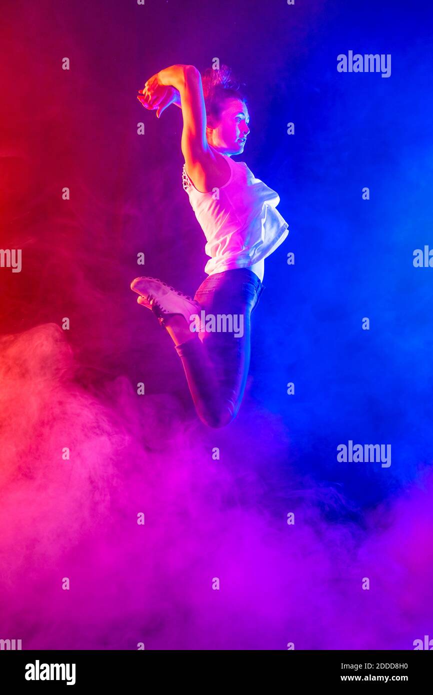Junge Frau springt mitten in der Luft zwischen rosa und blauem Rauch Stockfoto
