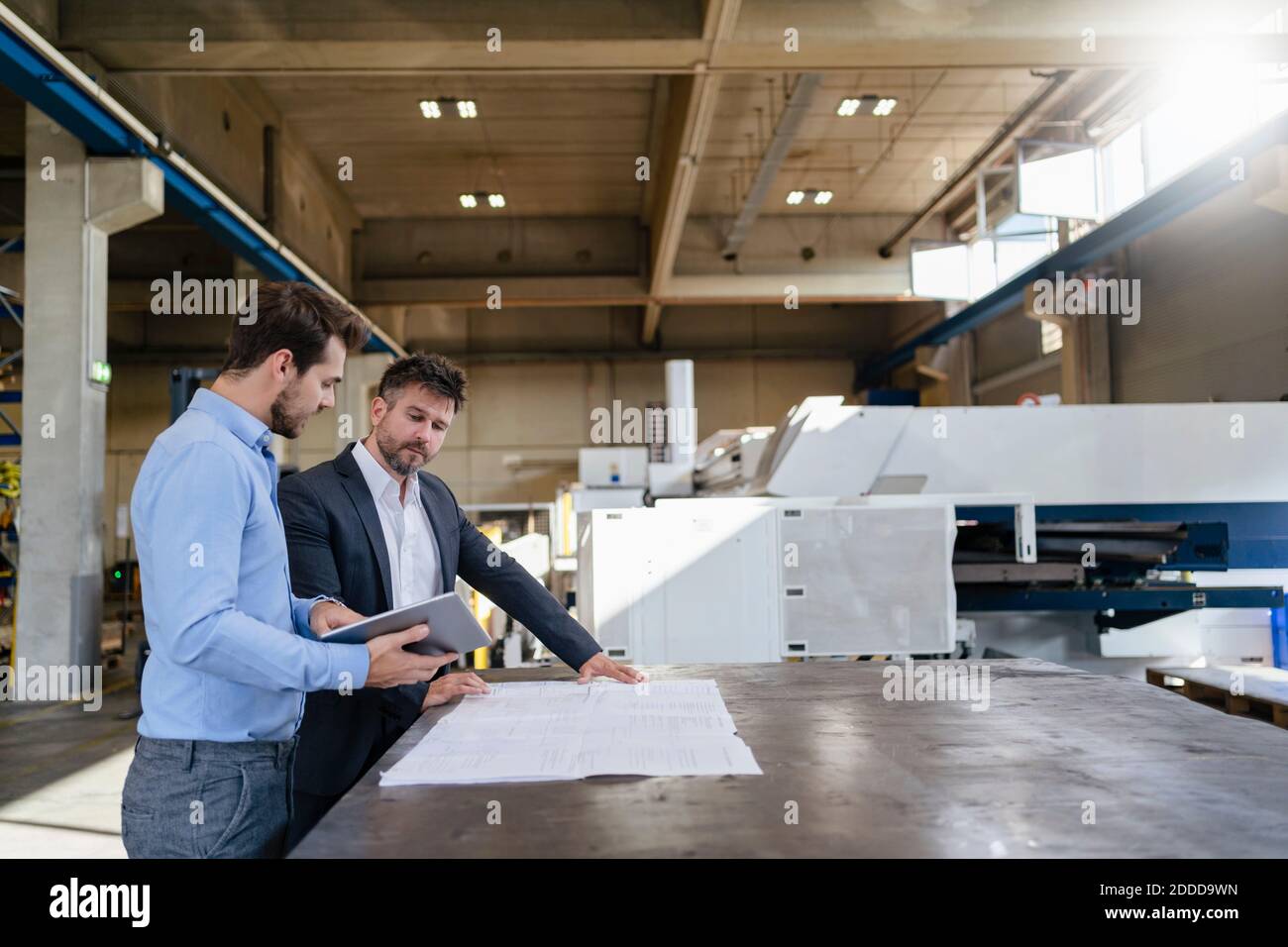 Geschäftsleute mit digitalem Tablet und blauem Druck stehen im Werk Stockfoto