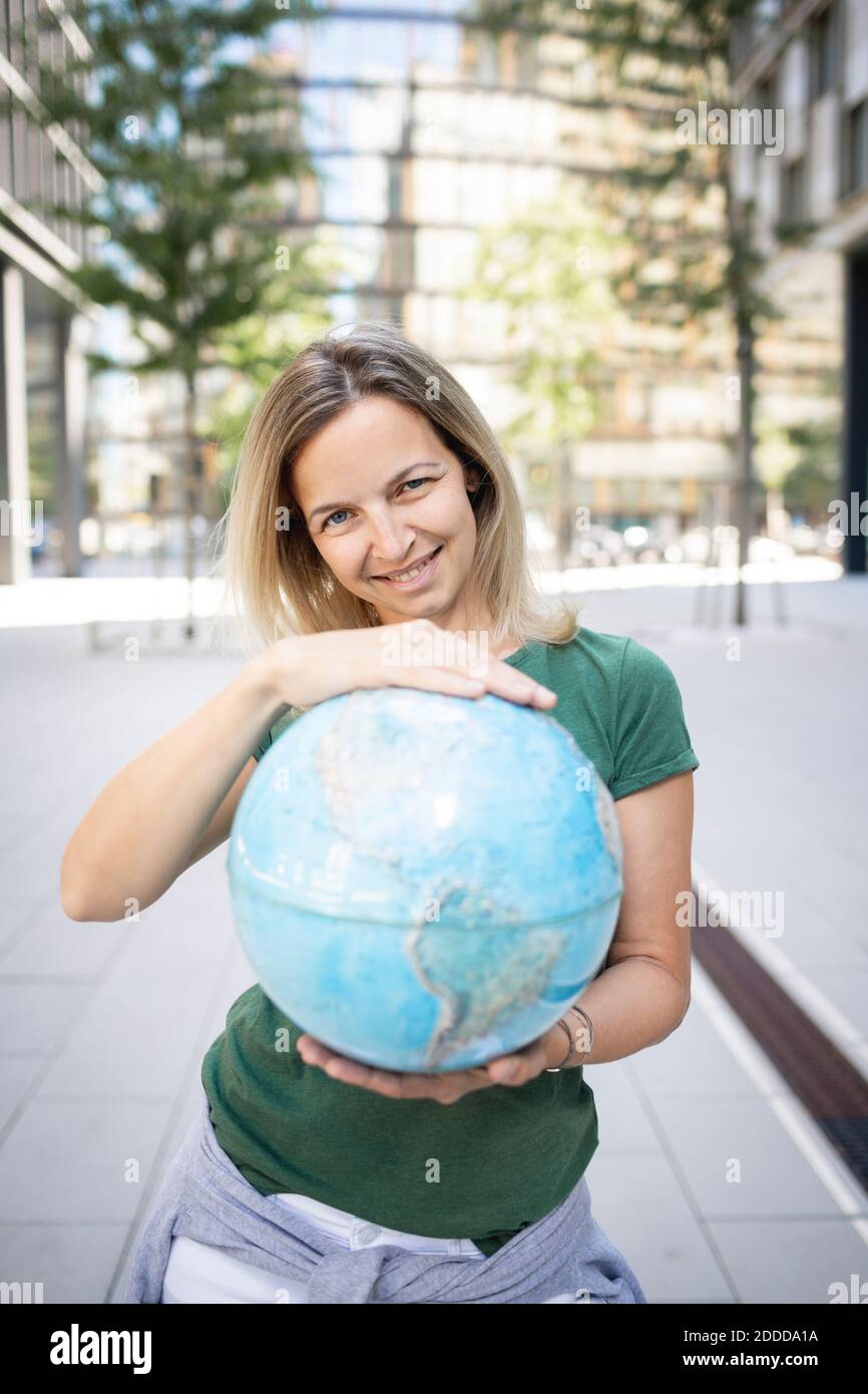 Mittlere Frau hält Globus, während sie auf dem Fußweg in der Stadt steht Stockfoto