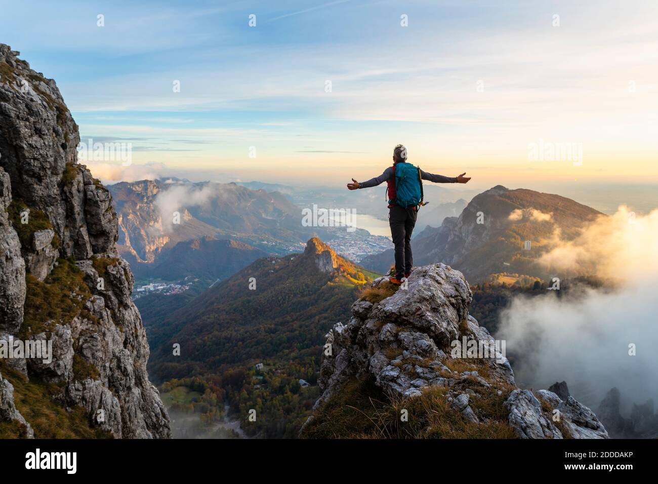 Nachdenklicher Wanderer mit ausgestreckten Armen, der während des Sonnenaufgangs in den Bergamasque Alps, Italien, auf dem Berg steht Stockfoto