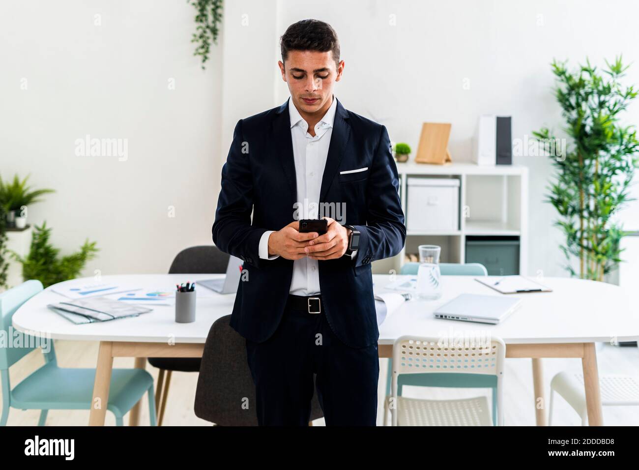 Gut aussehende junge professionelle Textnachrichten, während sie gegen den Schreibtisch stehen Kreativer Arbeitsplatz Stockfoto