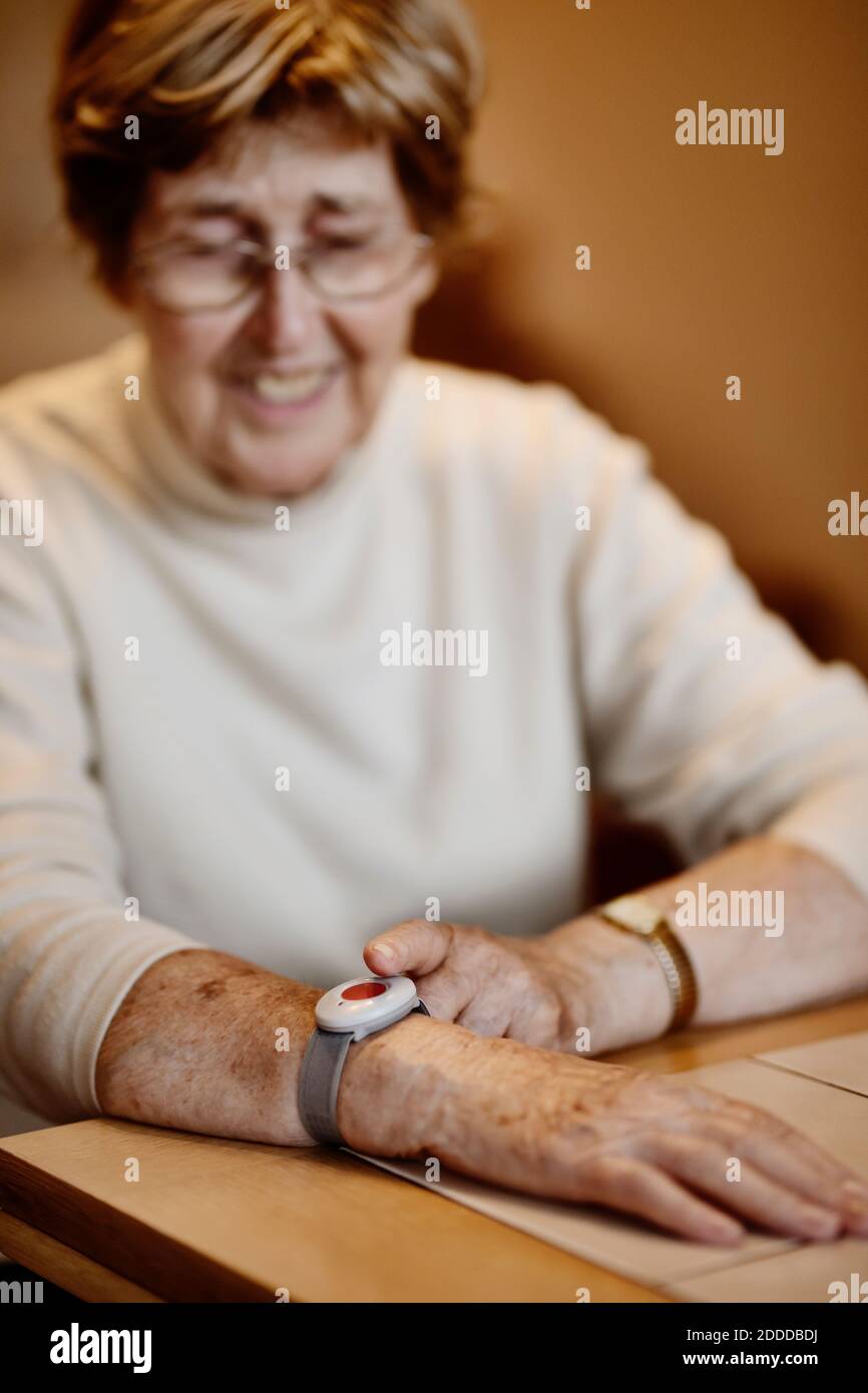 Ältere Frau, die den Notausschalter am Handgelenk über den Tisch drückt Zu Hause Stockfoto