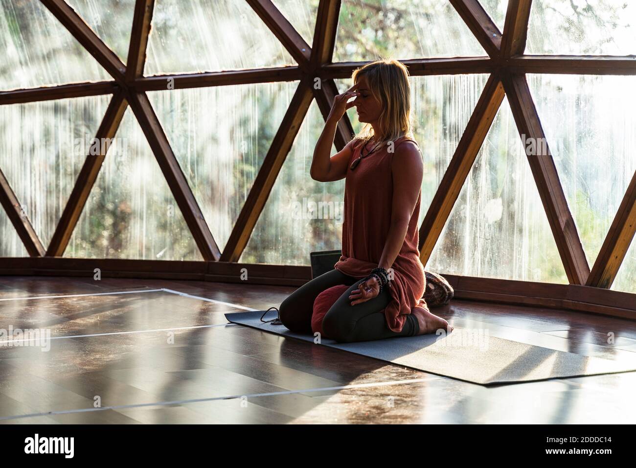 Reife Frau meditiert auf Yogamatte gegen Fenster bei Gesundheit Spa Stockfoto