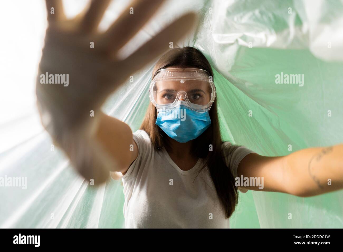 Frau trägt schützende Gesichtsmaske tun Stop-Geste, während bedeckt In Plastik während Coronavirus Stockfoto