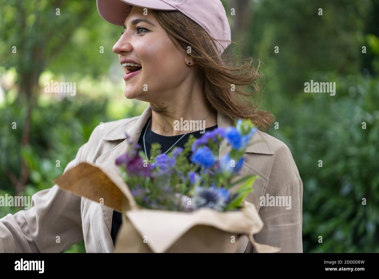 Junge Frau schaut weg mit Mund offen hält Bouquet während Im Park stehend Stockfoto