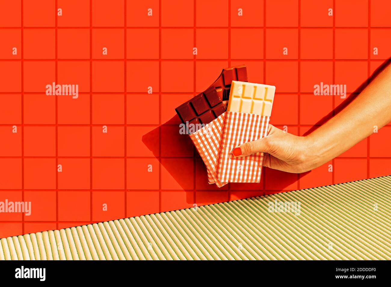 Weibliche Hand hält Schokoladenriegel an der roten Fliesenwand Stockfoto