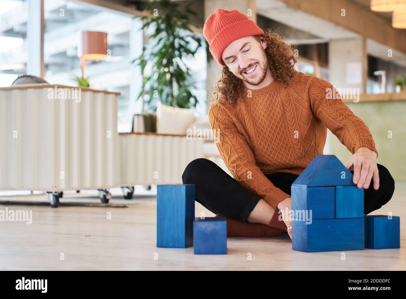 Hipster Mann spielt mit Spielzeugblock, während er auf dem Boden sitzt Im Wohnzimmer zu Hause Stockfoto