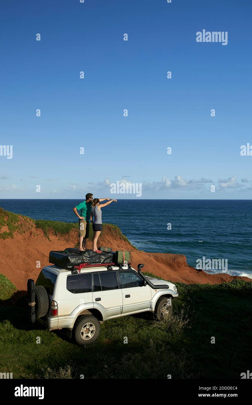 Paar zeigt, während man auf dem 4x4 Dach steht, während man anschaut Meer gegen blauen Himmel Stockfoto