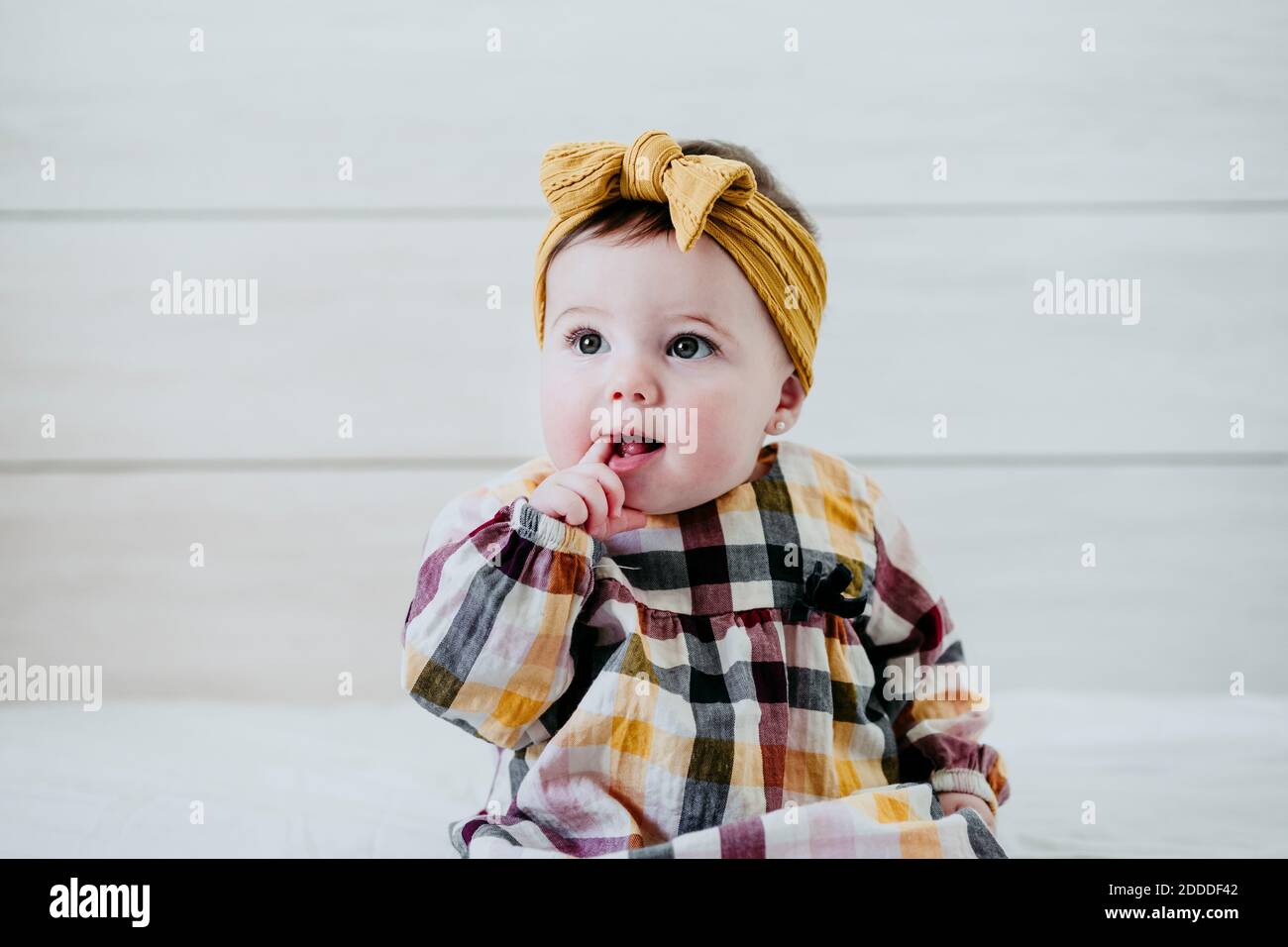 Baby Mädchen mit Finger im Mund sitzt auf dem Bett an Zu Hause Stockfoto