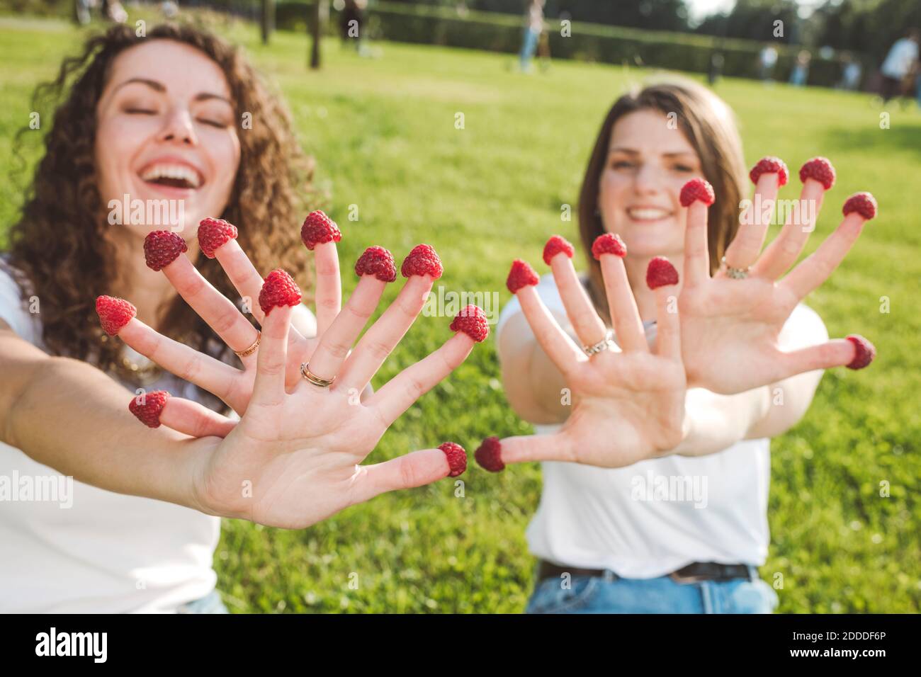 Spielerische Freundinnen genießen mit frischen Himbeeren an den Fingern parken Sie an sonnigen Tagen Stockfoto