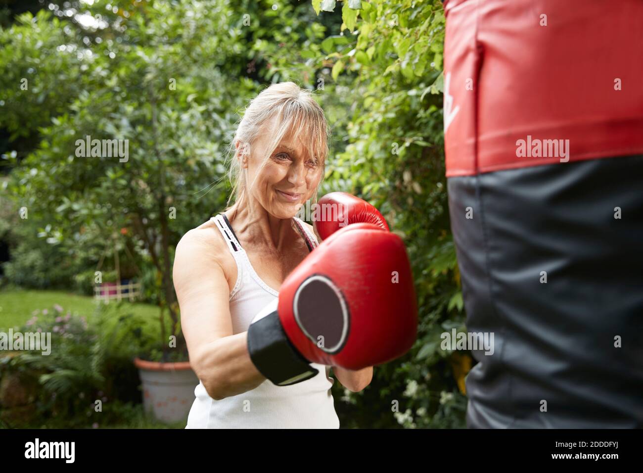 Ältere Frau, die im Hinterhof steht und einen Boxsack boxt An sonnigen Tag Stockfoto