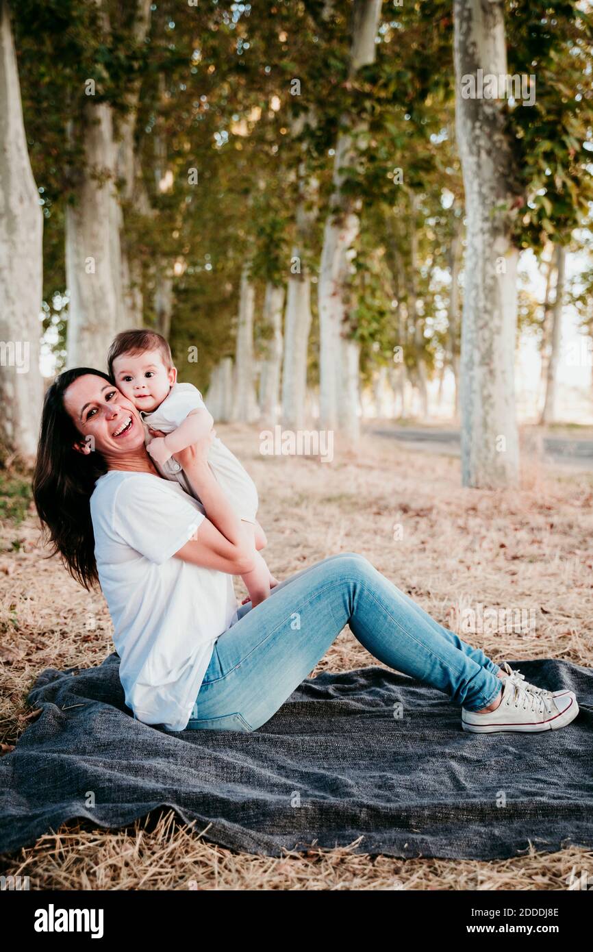 Lächelnde Mutter, die mit Baby spielt, während sie draußen auf der Decke sitzt Stockfoto