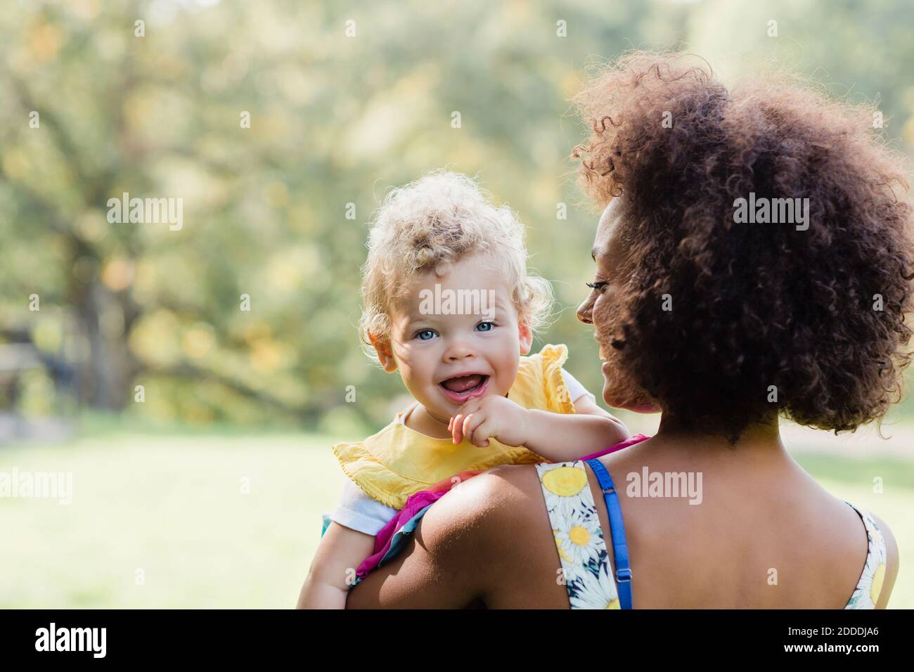 Mutter trägt lächelndes Baby, während sie im Park steht Stockfoto