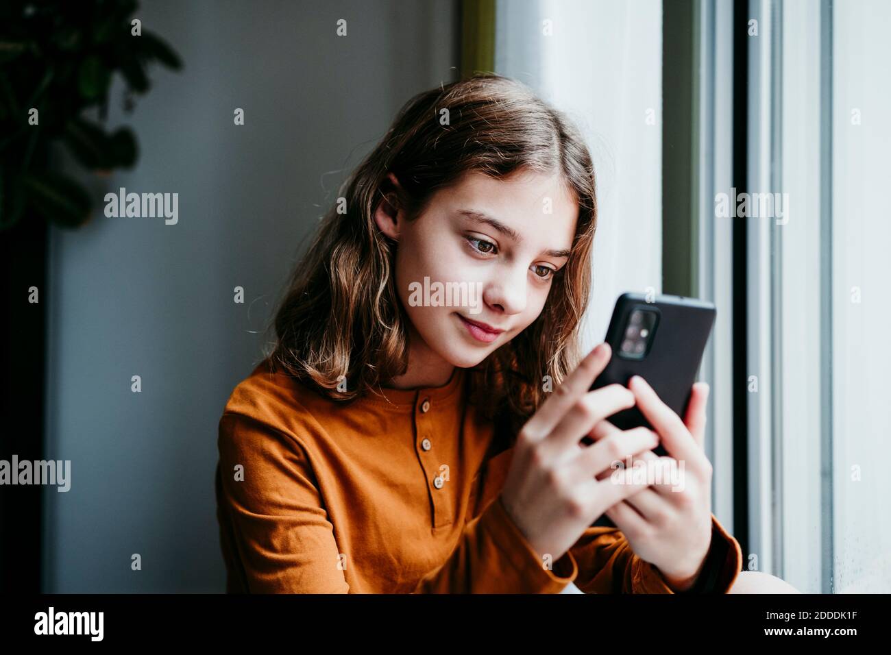 Vorpubertär Kind mit Handy, während sitzen am Fenster Zu Hause Stockfoto