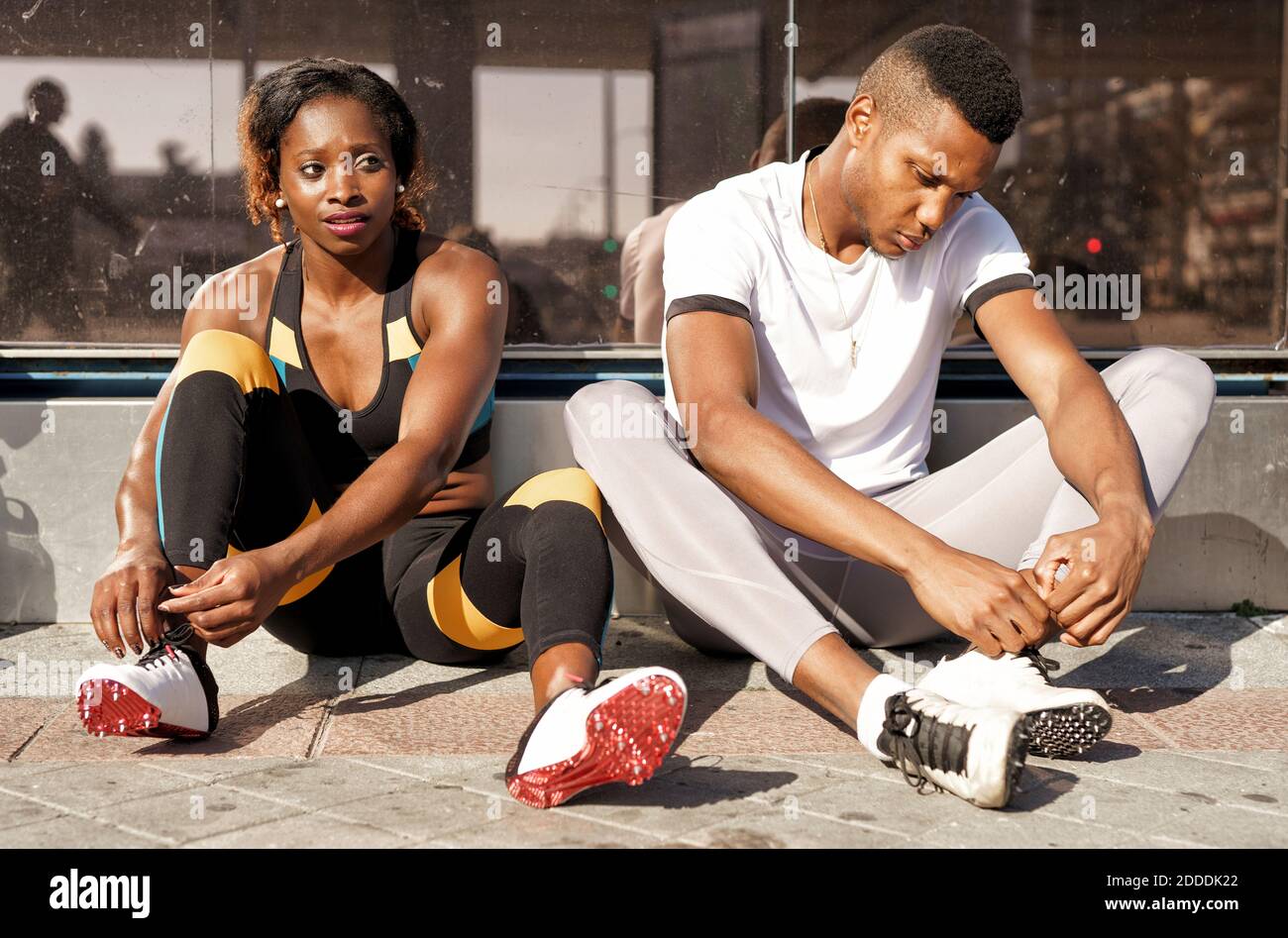 Sportler binden Schnürsenkel, während sie auf dem Bürgersteig in der Stadt sitzen Stockfoto