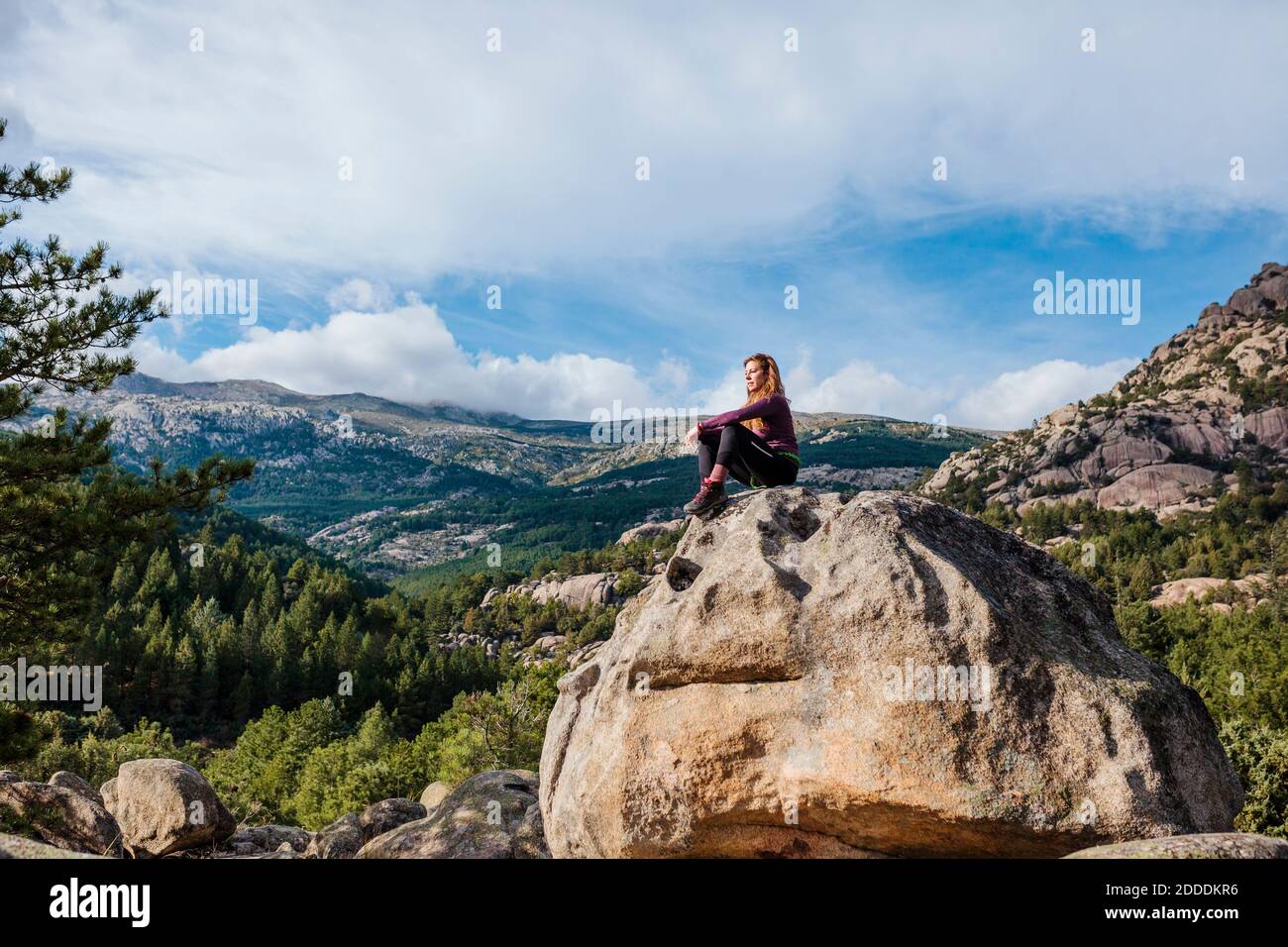 Trekker mit Blick auf den Blick, während er auf Felsen gegen Himmel in La Pedriza, Madrid, Spanien sitzt Stockfoto