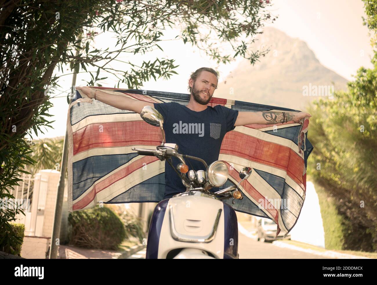 Mann mit ausgestreckten Armen hält Nationalflagge, während er sitzt Motorrad im Sommer Stockfoto