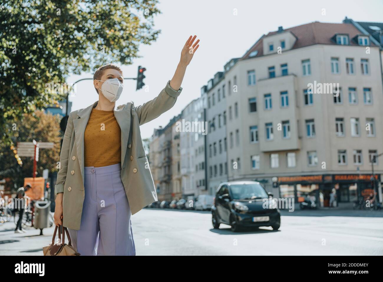 Frau trägt schützende Gesichtsmaske rufen Taxi durch winken stehen Auf der Straße in der Stadt Stockfoto