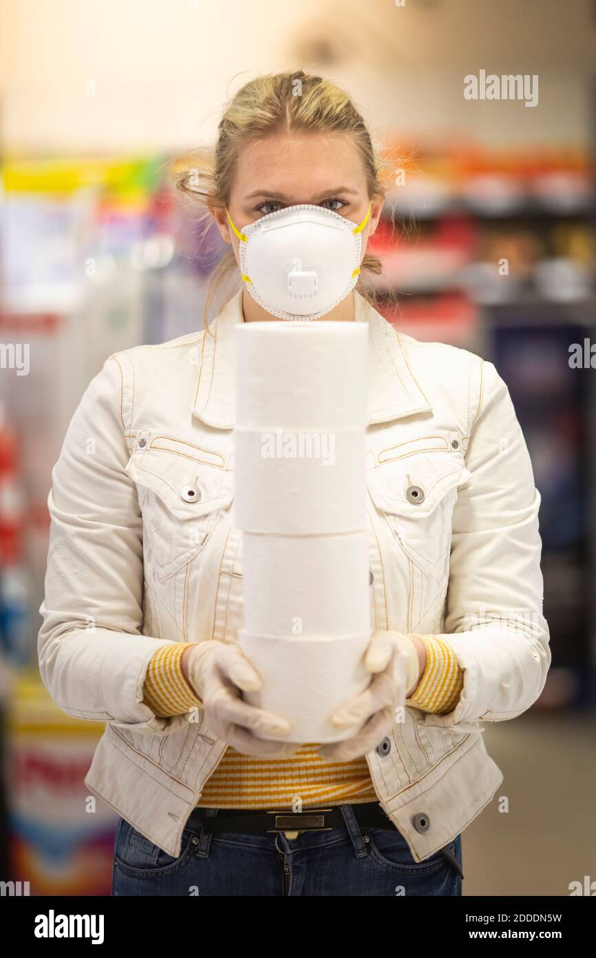 Teenager-Mädchen tragen Schutzmaske und Handschuhe halten Stapel von Vier Toilettenrollen im Supermarkt Stockfoto