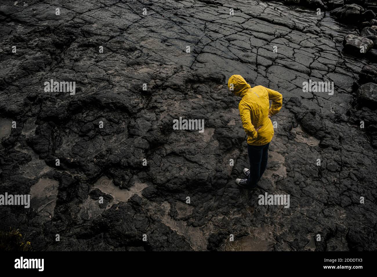 Drohne Aufnahme einer Frau, die Regenmantel trägt, während sie auf Felsen steht Boden während der Regenzeit Stockfoto