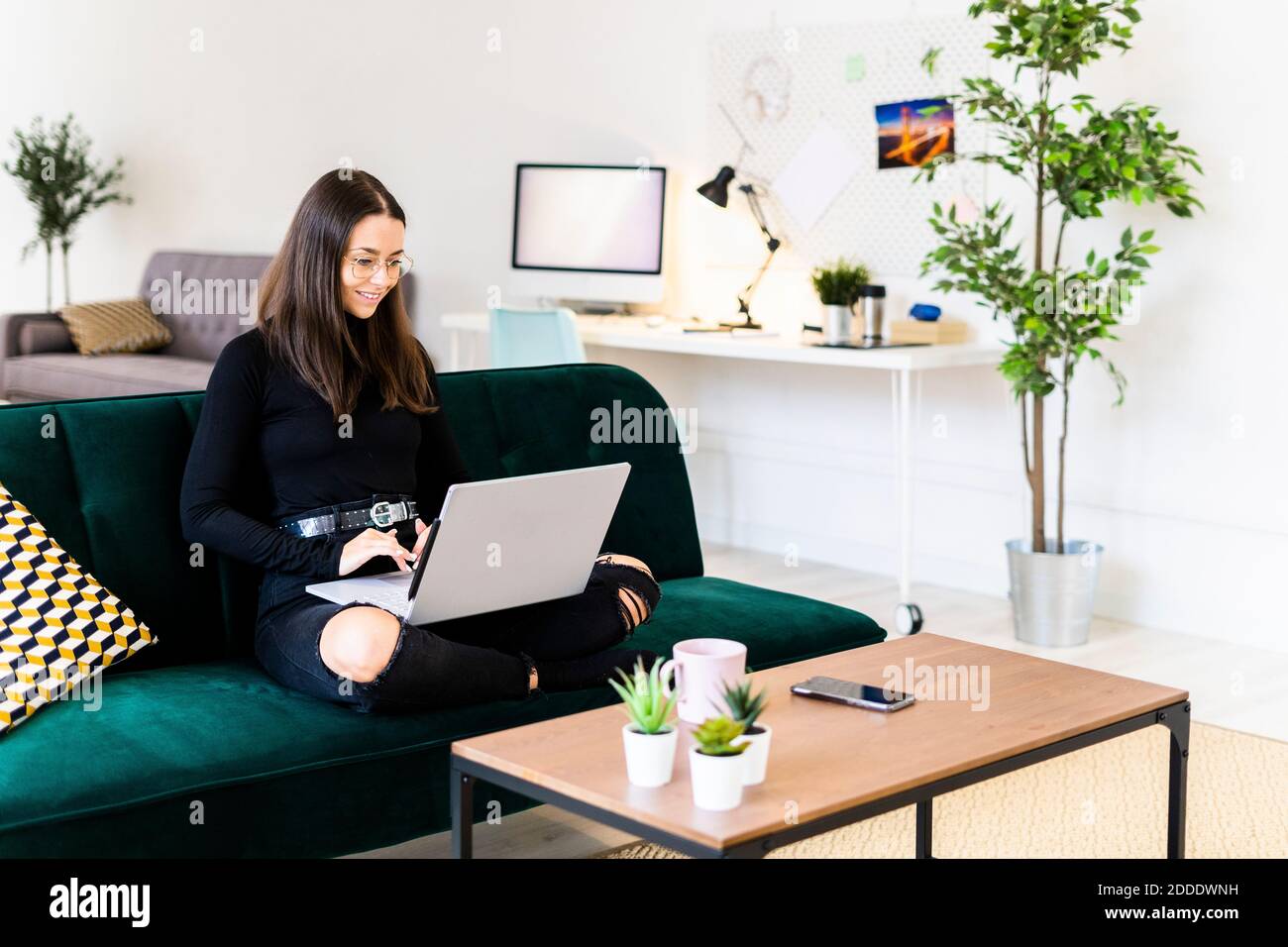 Lächelnd schöne junge Frau mit Laptop zum Bloggen während des Sitzens Auf dem Sofa zu Hause Stockfoto