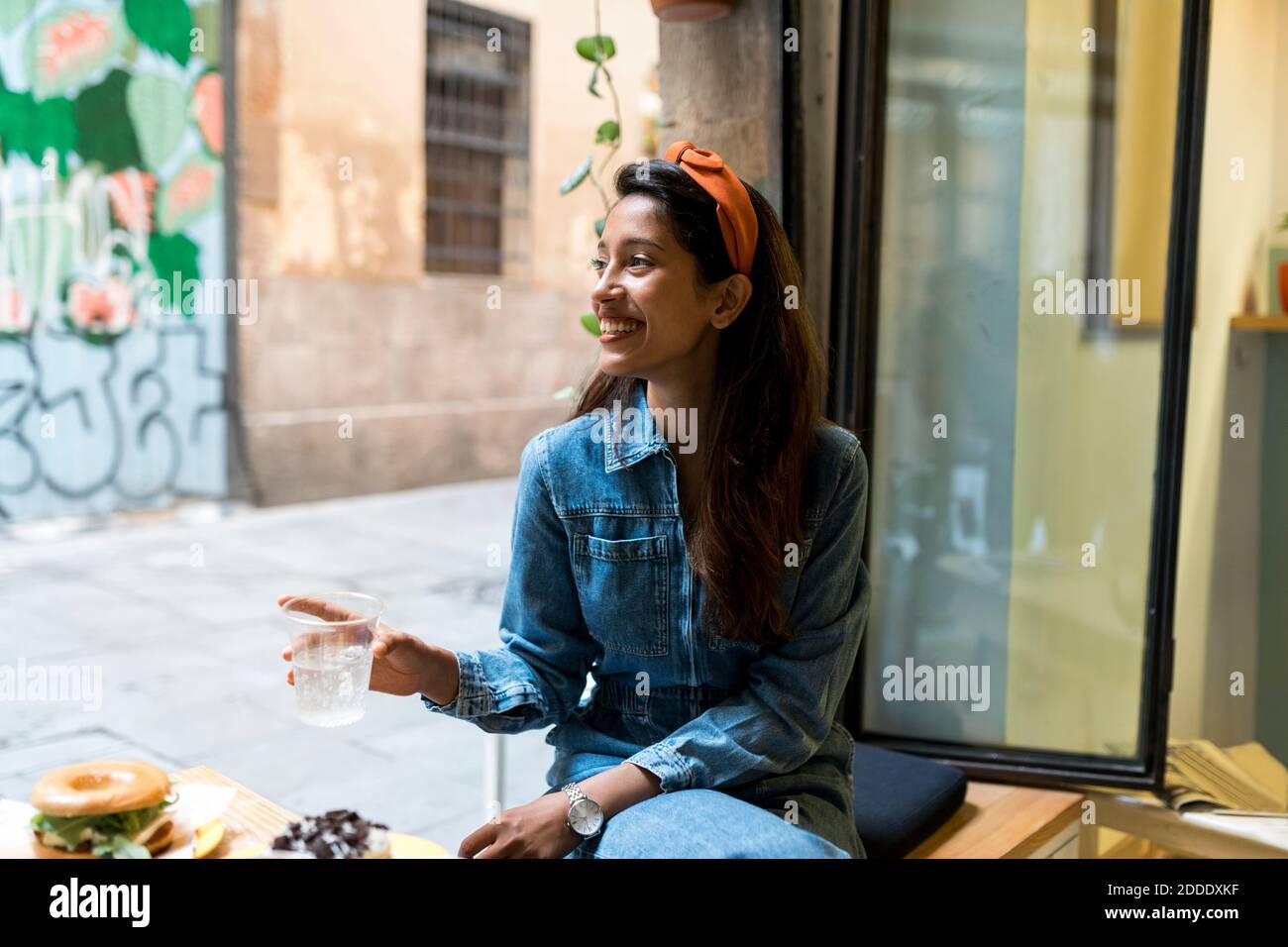 Lächelnde junge Frau, die beim Essen am Fenster sitzt Café Stockfoto