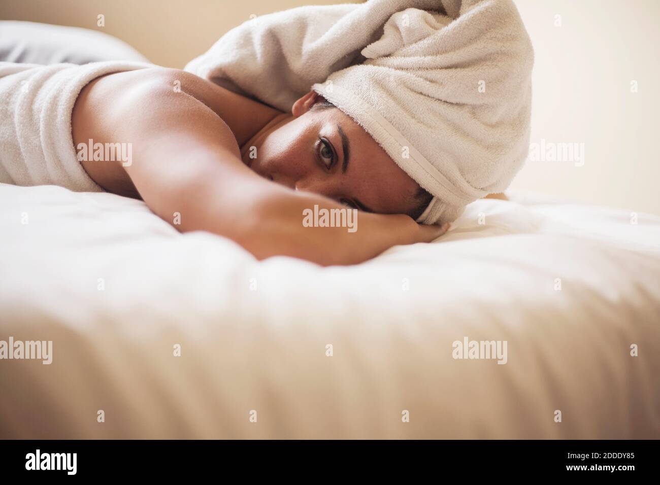 Junge Frau mit nassem Haar in Handtuch liegend gewickelt Auf dem Bett zu Hause Stockfoto