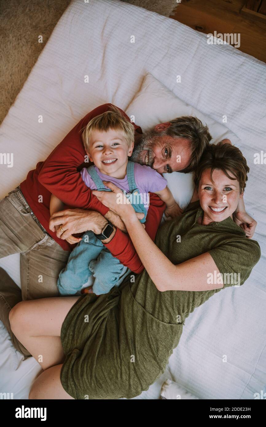 Mutter, Vater und Sohn umarmen sich gegenseitig, während sie zu Hause auf dem Bett liegen Stockfoto