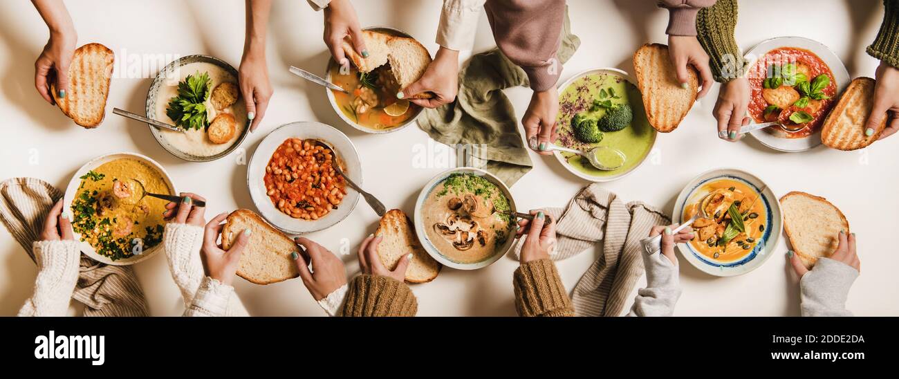 Menschen essen Herbst und Winter cremige vegane Suppen. Flache Hände, Suppenteller und Brotscheiben auf weißem Tischhintergrund, Draufsicht. Herbst- und Wintermenü, vegetarische Gerichte Stockfoto