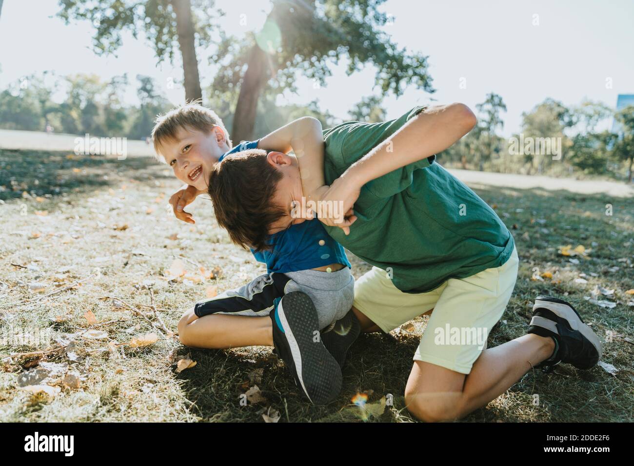 Lächelnde Brüder umarmen einander im öffentlichen Park auf sonnig Tag Stockfoto