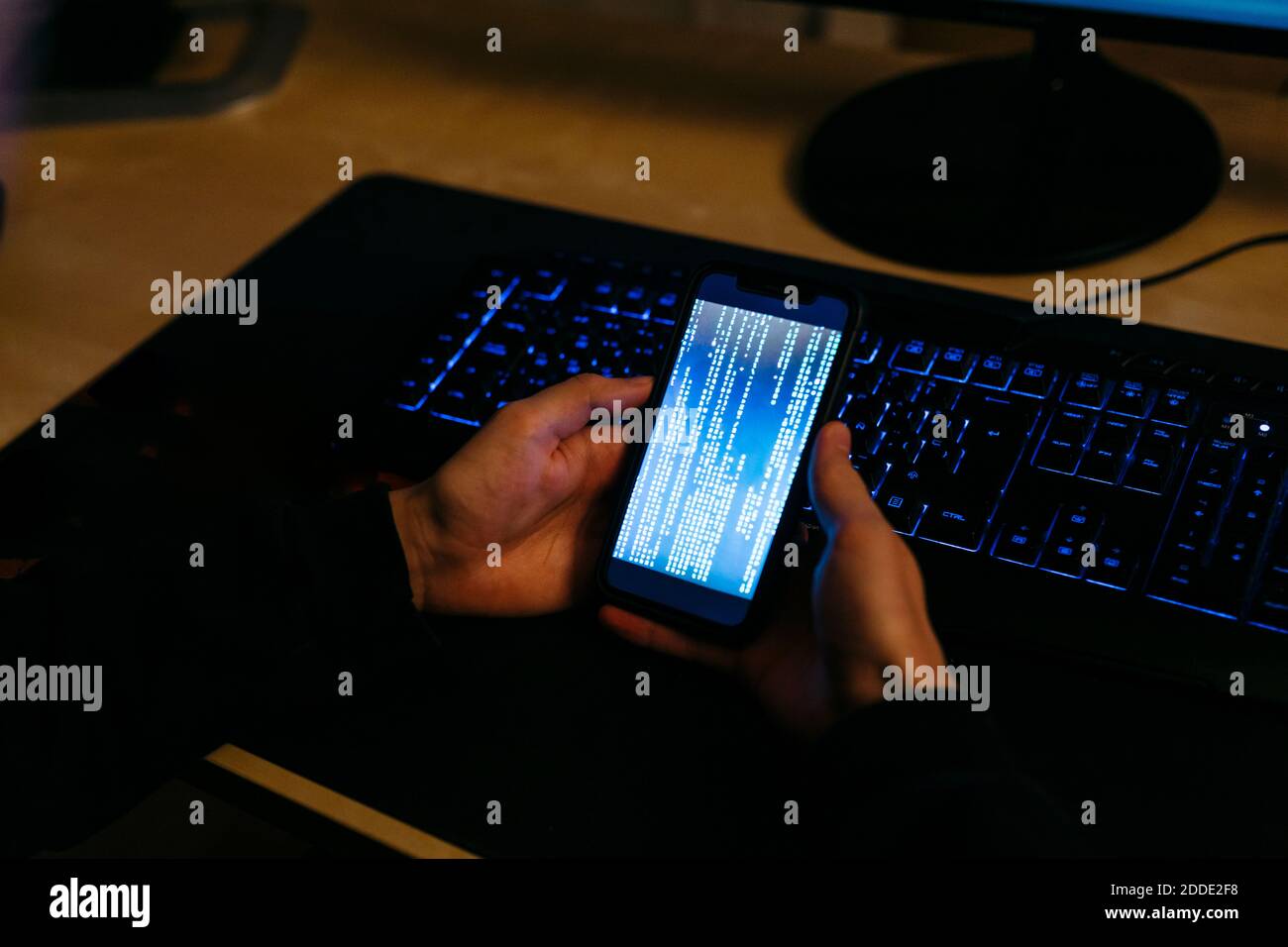 Hacker, der während der Arbeit im Büro ein Mobiltelefon zum Programmieren verwendet Stockfoto