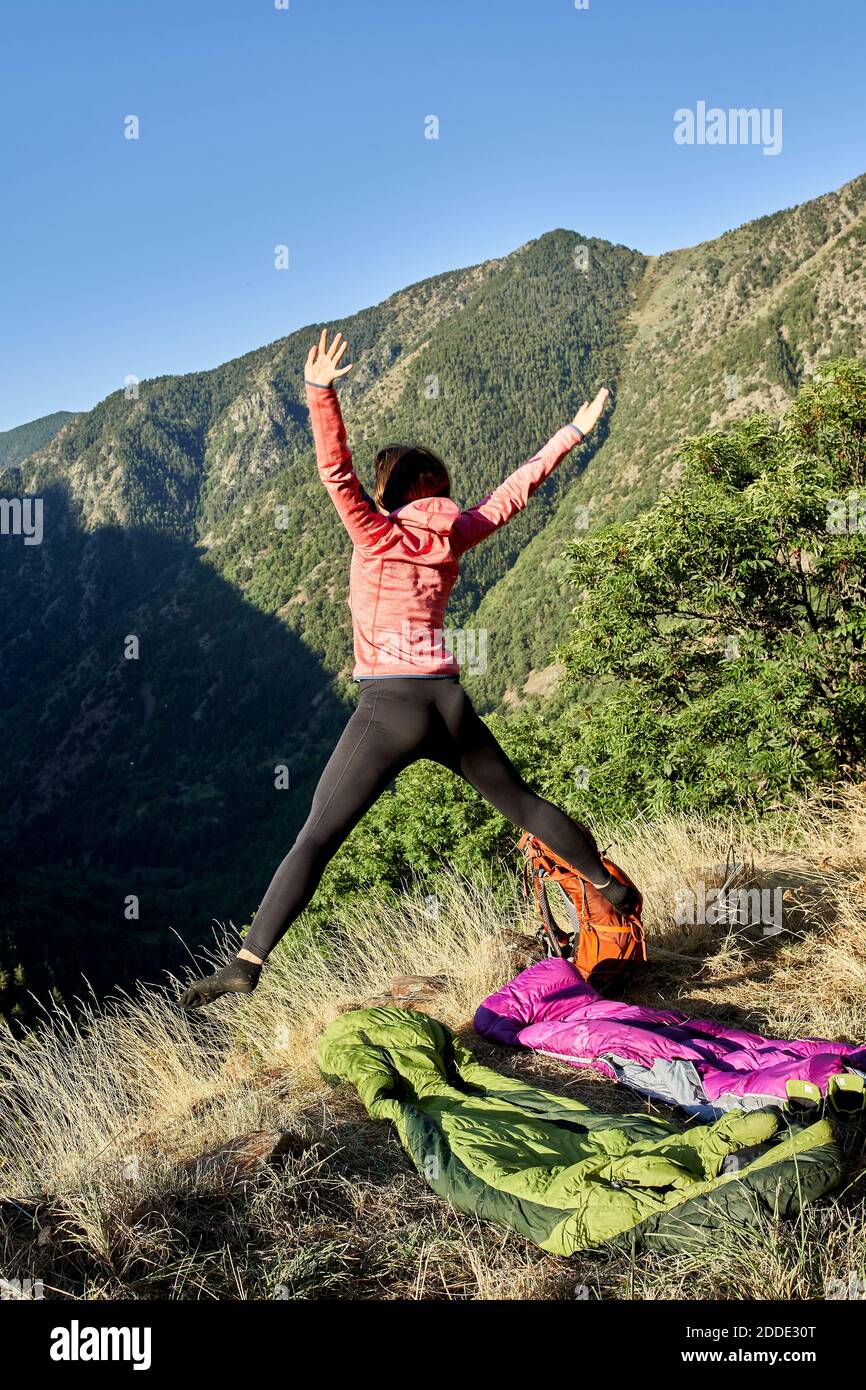 Mittlere Erwachsene Frau springen mit den Armen im Wald auf angehoben Sonniger Tag Stockfoto