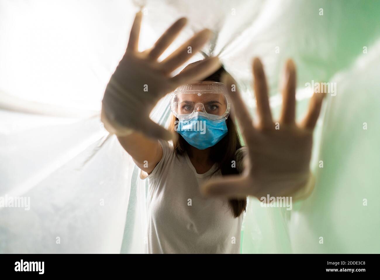 Frau trägt schützende Gesichtsmaske tun Stop-Geste, während bedeckt In Plastik während des COVID-19 Ausbruchs Stockfoto